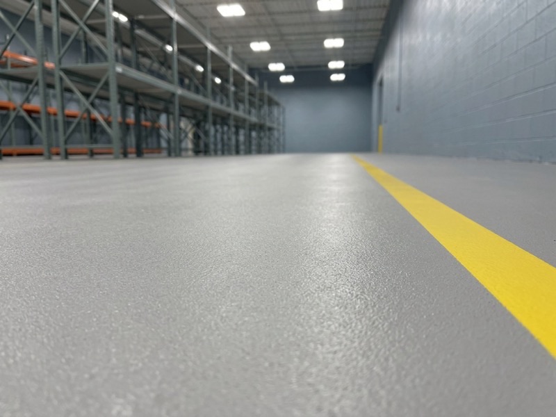 Light gray high-solids industrial epoxy warehouse floor with yellow safety striping
