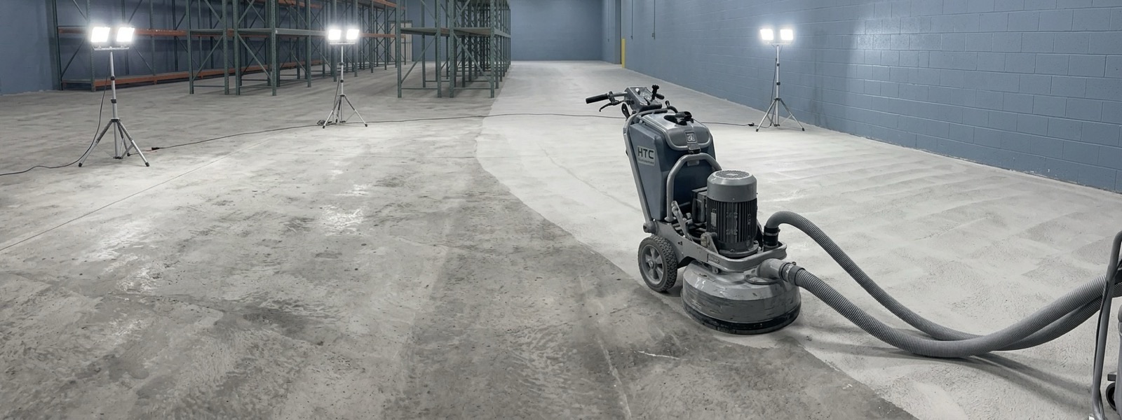 Walk-behind diamond grinder with dust shroud preparing a bare concrete slab before coating